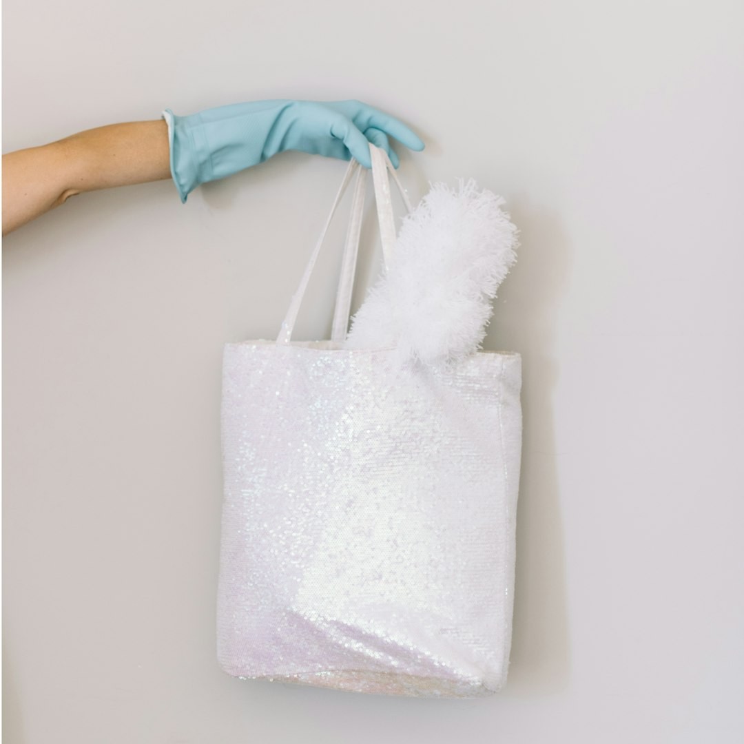 Woman in blue rubber cleaning glove holds up white sequin bag with a lambswool duster.